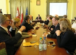 Radni klubu Platformy Obywatelskiej siedzą przy stole. W tle przy stole prezydialnym siedzi przewodniczący sejmiku Ludwik Rakowski