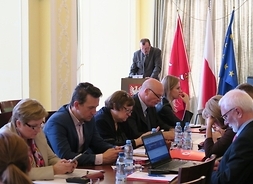 Przy stole siedzą radni Platformy Obywatelskiej. W tle przy mównicy przemawia wicemarszałek Wiesław Raboszuk