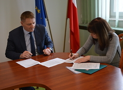 umowy podpisują marszałek Orzełowska i burmistrz Ciak, w tle flagi Polski i Unii