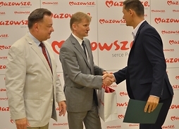 dyrektor Mazowieckiego Samorządowego Centrum Doskonalenia Nauczycieli Jarosław Zaroń gratuluje mężczyźnie wyróżnionemu w konkursie na scenariusz lekcji o Mazowszu