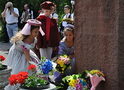Dzieci w strojach z epoki renesansu składają kwiaty pod pomnikiem Jana Kochanowskiego