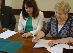 Stół, rozłożone dokumenty, Elżbieta Lanc składa podpis