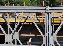 Przez kratownicowy bok widać robotników na powierzchni nowego mostu