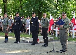 Grupa harcerzy i strażników miejskich, wygłaszający apel przy mikrofonie