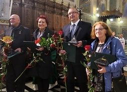 Czworo nagrodzonych z kwiatami i statuetkami przed ołtarzem katedry w Płocku