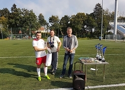 Zawodnicy trzymający nagrody i dyplomy na boisku do gry w piłkę nożną.