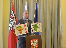 dyrektor trzyma w dłoni dwie mapy Mazowsza z zaznaczonymi obszarami gdzie wystęuje smog