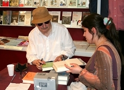 Pisarz przy stoliku w letniej koszuli oraz charakterystycznych okularach i kapeluszu