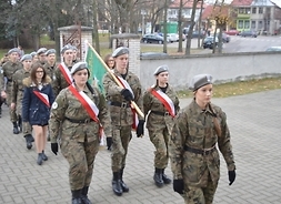 Uczniowie w mundurach niosą sztandar szkoły