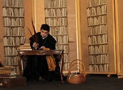 Scena z przedstawienia - chłopiec w todze i z piórem w dloni siedzi za biurkiem