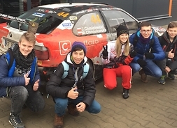 Czterech uczniów pozuje do zdjęć z Moniką Chmielewską, żoną i zarazem pilotem Jana Chmielewskiego przed samochodem marki BMW należącym do Chmielewski Team