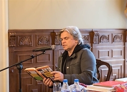 Aktor czytający przez mikrofon książkę „Dynastia Niziołków”