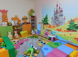 Pokój zabaw w żłobku. Widać kolorowe meble i zabawki, a na ścianie fototapetę z zamkiem z bajki