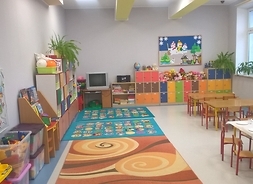 Zdjęcie przedstawia jedną z sal przedszkola. Widać kolorowy dywan i szafki z zabawkami