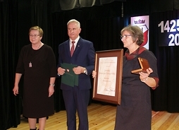 Przewodnicząca Bożena Pacholczak stoi obok przedstawicieli uniwersytetu, którzy trzymają dyplom
