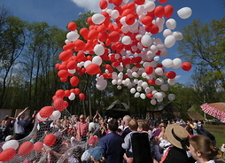Ponad głowami ludzi unoszą się wypuszczone balony w kolorze białym i czerwonym.