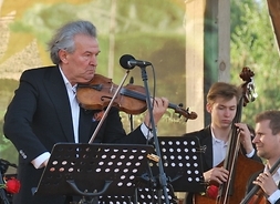 skrzypek Vadim Brodski gra na skrzypcach, w tle orkiestra Mazowieckiego Teatru Muzycznego