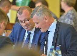 Wicemarszałek Wiesław Raboszuk i członek zarządu Rafał Rajkowski siedzą zwróceni ku sobie, w ręku trzymają dokumenty