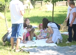 Dzieci siedzą na kocu na trawie i rysują