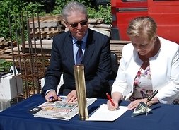 dwie osoby siedzą przy stole, w tym członek zarzadu Elżbieta Lanc i podpisują akt erekcyjny pod budowę stacji
