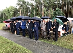 uczestnicy uroczystości stoją z rozłożonymi parasolami