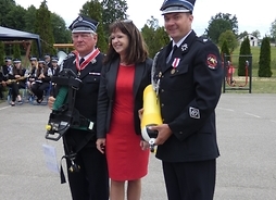 Wicemarszałek Janina Ewa Orzełowska stoi z ochotnikami. Strażacy trzymają aparat ODO