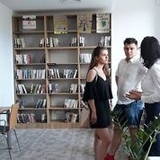 Trzy młode osoby rozmawiają, w tle półki z książkami