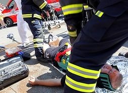 Strażacy podczas akcji ratowniczej. Jeden ze strażaków pochyla się nad rannym