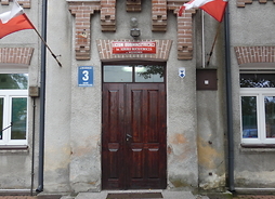 Wejście do budynku szkoły. Widać drewniane drzwi i flagi
