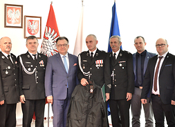 Strażacy wraz z marszałkiem pozują do zdjęcia na tle flag Polski, UE i województwa mazowieckiego
