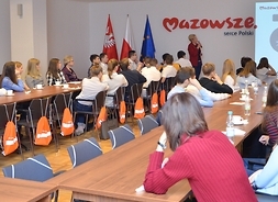 dyrektor Departamentu Kultury, Promocji i Turystyki Izabela Stelmańska stoli przy tablicy, gdzie wyświetlana jest prezentacja o Mazowszau, wokół po obu stronach przy stołach siedzi młodzież gimnazjalna