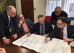 marszałek Adam Struzik i samorzadowcy z powiatu pruszkowskiego rozmawiają nad rozłożoną mapą z oznaczonymi ciągami komunikacyjnymi na obszarze powiatu pruszkowskiego