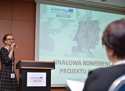 dyrektor Katarzyna Wieczorek z mikrofonem w ręku stoi przed uczestnikami konferencji podsumowującej projekt Rumobil