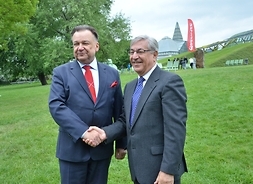 komisarz Karmenu Vella i marszałek Adam Struzik w uścisku dłoni, t tle ogrody niwesyteckiej bibblioteki