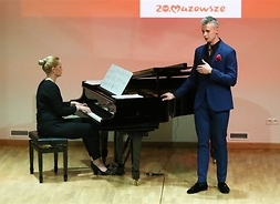 Artysta w podczas występu na scenie. Towarzyszy mu pianistka grająca na instrumencie muzycznym