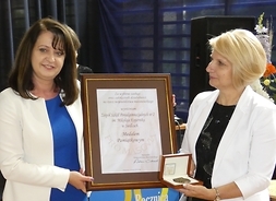 Dwie kobiety stoją obok siebie i trzymają dyplom oprawiony w ramki