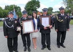 Trzej druhowie OSP w Rudzienku stojący obok członka zarządu województwa Janiny Ewy Orzełowskiej prezentują Medal Pamiątkowy „Pro Masovia”