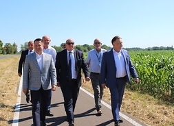 Marszałek i radny Orliński wraz z czterema panami idą nową ścieżką pieszo-rowerową. Na pierwszym planie marszałek i radny