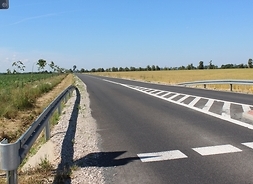 Widok na pustą wyremontowaną drogę. Na jezdni widać namalowane białe linie, które są częścią oznakowania ulicy