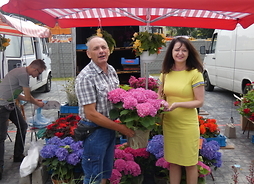 stragan z kwiatami na targowisku, z kwiatami w ręku stoi włąściciel straganu, obok członek zarządu Janina Ewa Orzełowka