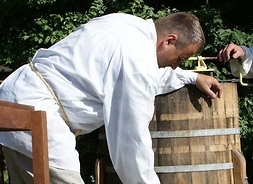 Męzczyzna upuszczający ciekły miód do glinianego dzbanka z drewnianej beczki. Zdjęcie plenerowe