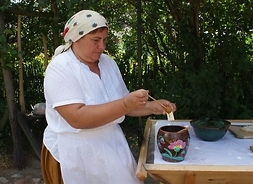 Kobieta nabierająca miód specjalną drewnianą pałeczką z glinnego dzbana, stojącego na stole. Zdjęcie wykonane w plenerze