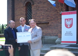 marszałek Adam Struzik, proboszcz kościoła parafialnego w Dobrzykowie trzymają certyfikat