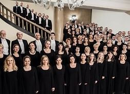Kilkudziesięcioro członków chóru Filharmonii Narodowej stoi w kilku rzędach pozując do fotografii.