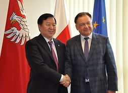 Prezes Zarządu Centrum Handlu Zagranicznego Chin w Kantonie Li Jinqi i marszałek Adam Struzik  podają sobie ręce na tle flag polskiej i UE