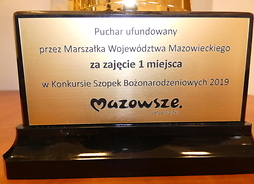 Drewniana tabliczka z podparciem, na której jest napisane nazwa konkursu, numer zajętego miejsca oraz nazwa współorganizatora i logo Mazowsza