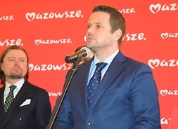 Mówi do mikrofonu stojąc prezydent Warszawy Rafał Trzaskowski, za nim stoi jeden z uczestników konferencji.