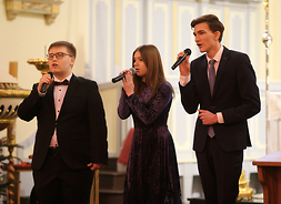 Trzech młodych muzyków z mikrofonami w dłoniach śpiewa kolędy