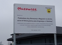 Widok stojącej na dwóch metalowych wspornikach tablicy informującej o zakończonej inwestycji przebudowy ul. Słonecznej w Węgrowie.