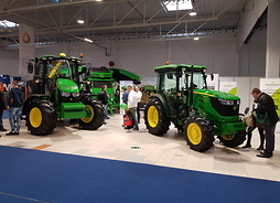 Hala targowa, na pierwszym planie trzy nowoczesne traktory średniej wielkości koloru zielonego.
